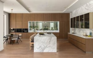 Modern kitchen with a marble island and wooden cabinetry, featuring a cozy dining area.