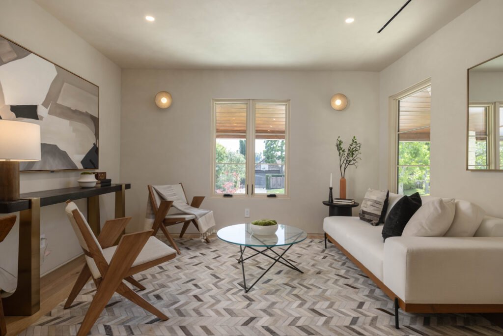 Modern living room with geometric rug, wooden chairs, glass table, and abstract art. Cozy and minimalist interior design.