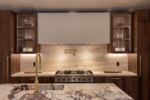 Luxurious modern kitchen with marble countertops, golden faucet, wooden cabinets, and stainless steel stove.